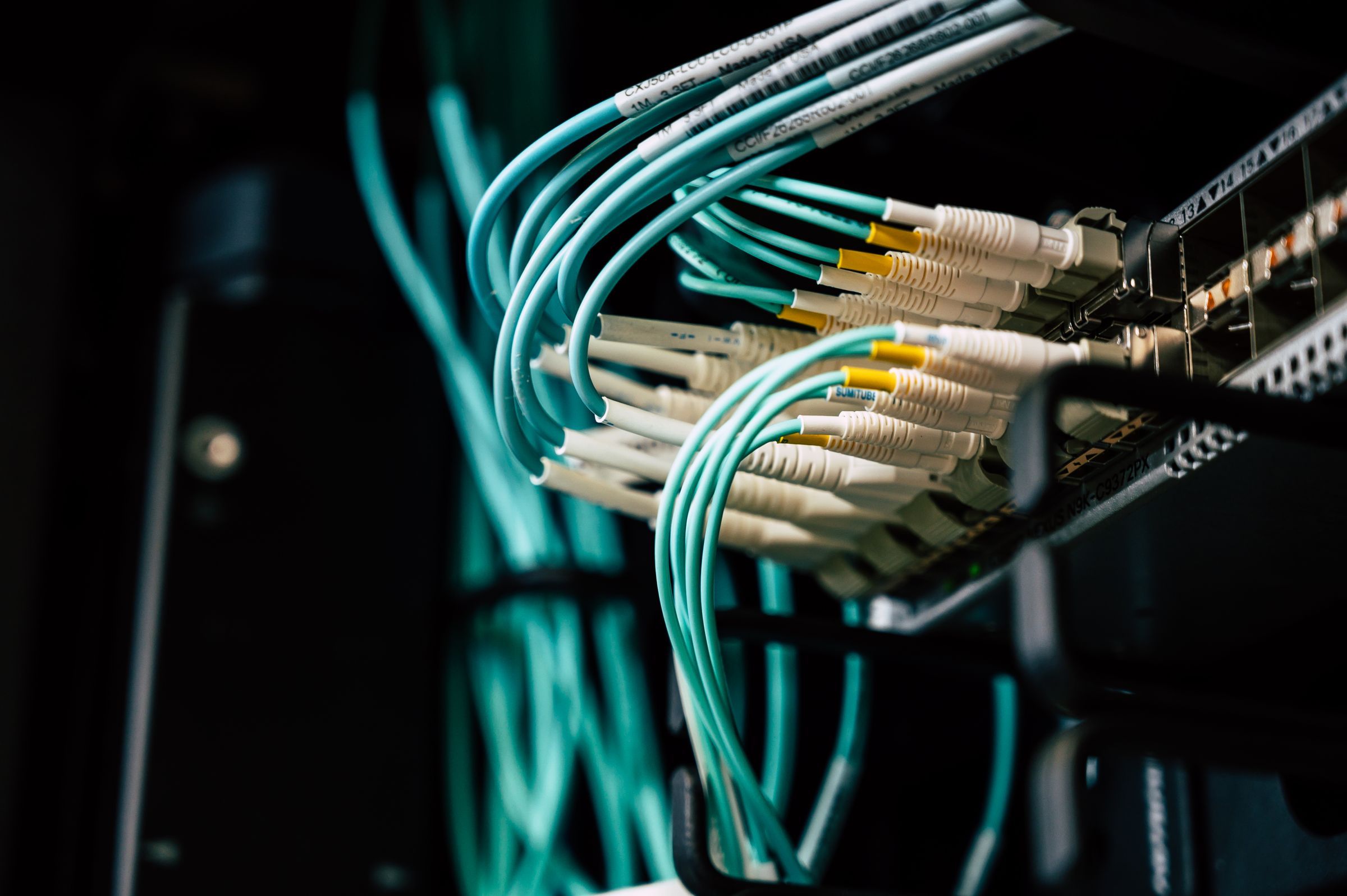 Glasfaserkabel in Türkis an einem Netzwerkschrank.